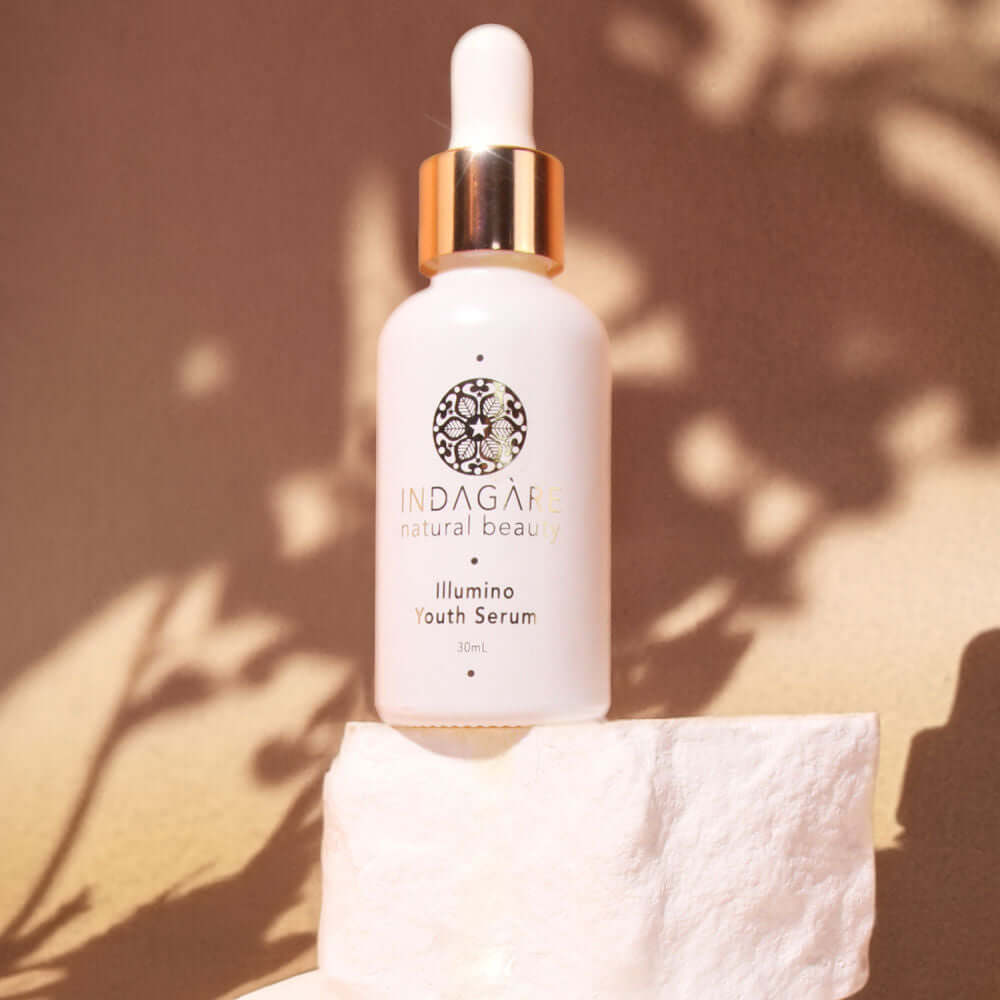 Indagare's Illumino Youth Serum photographed on a white shelf with the shadow of tree leaves in the background