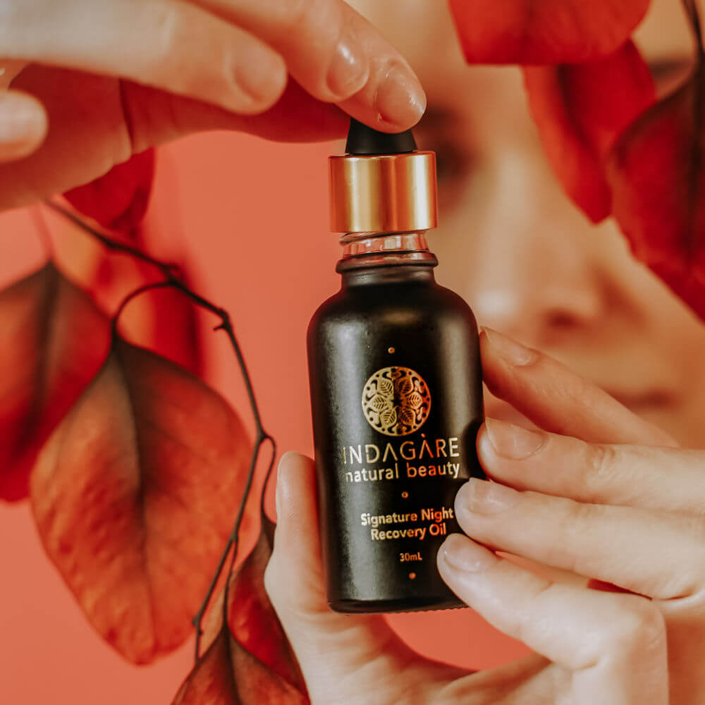 Woman's h ands holding the Signature Night Recovery oil against a backdrop of red autumn leaves