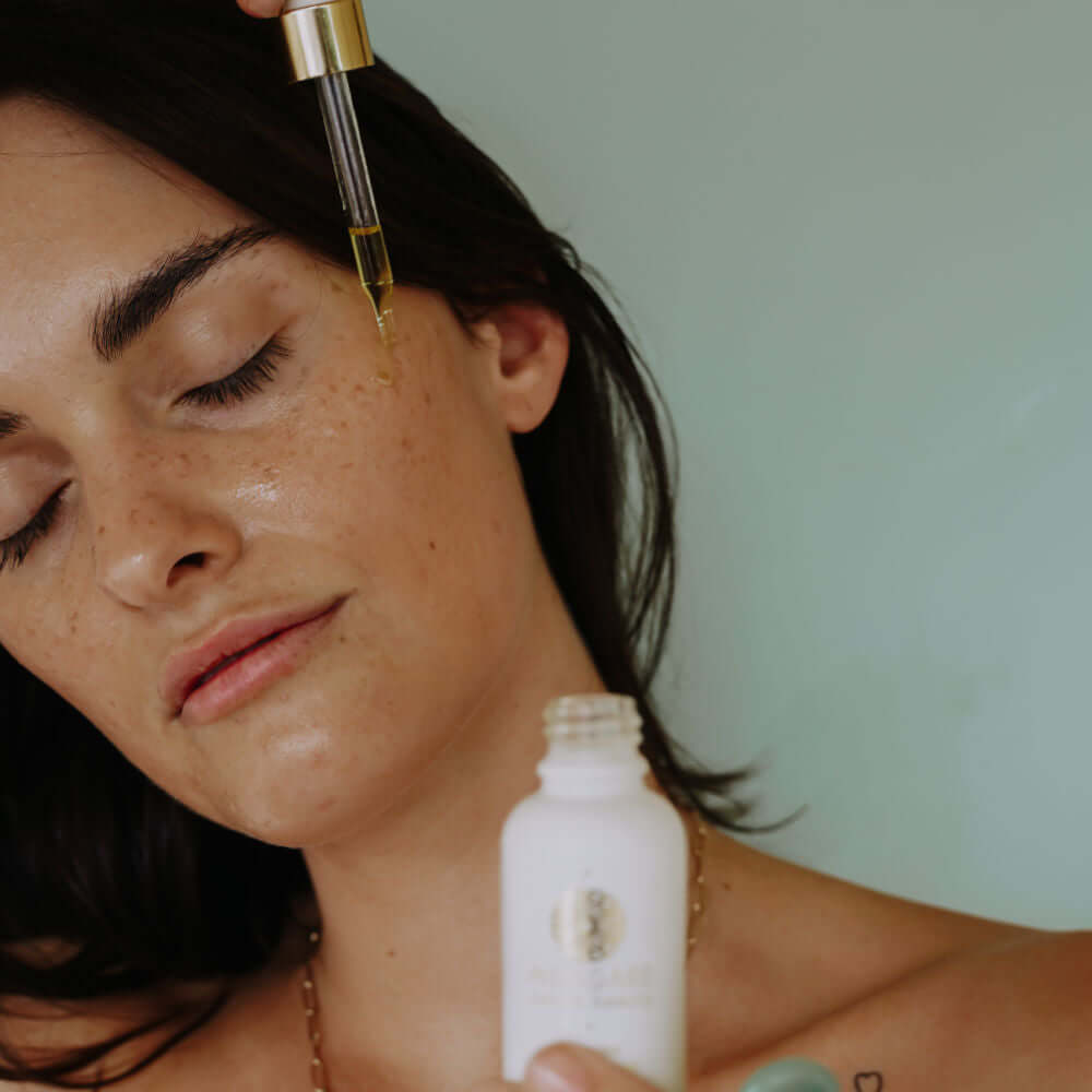 Woman holding Illumino Youth Serum face oil and dripping it onto her cheek