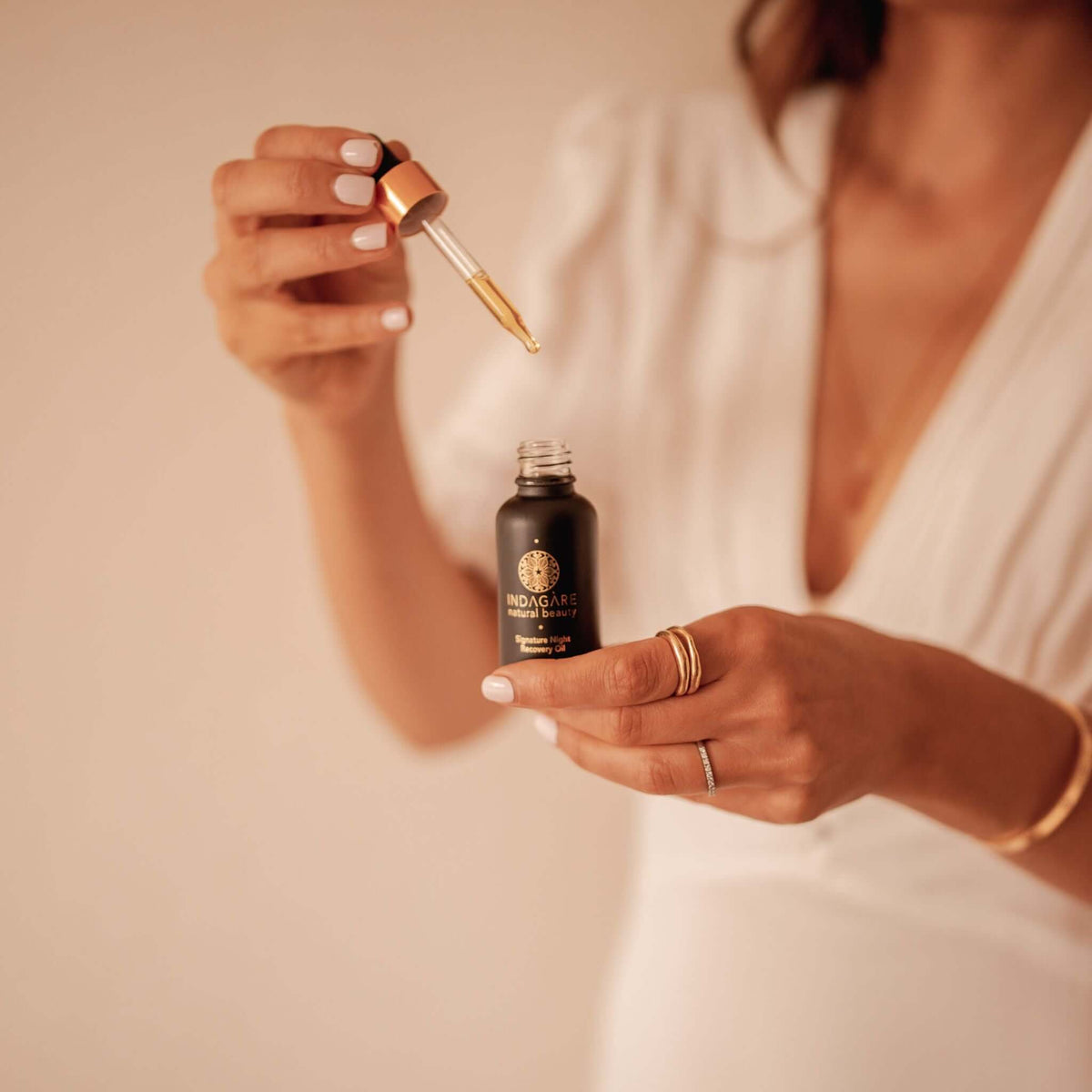 Woman holding Indagare's Signature Night Recovery Oil, dripping oil from dropper into bottle