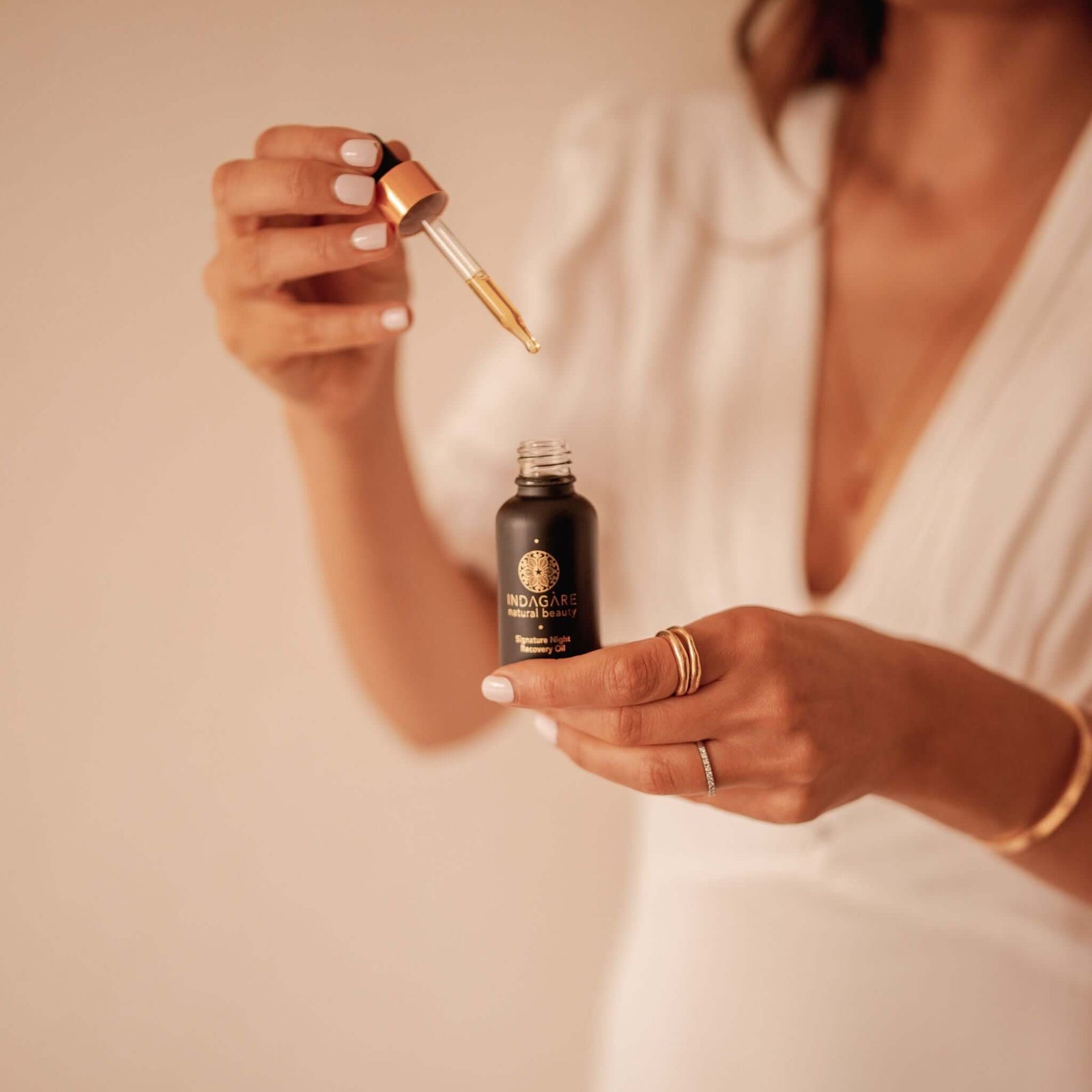 Woman holding Indagare's Signature Night Recovery Oil, dripping oil from dropper into bottle