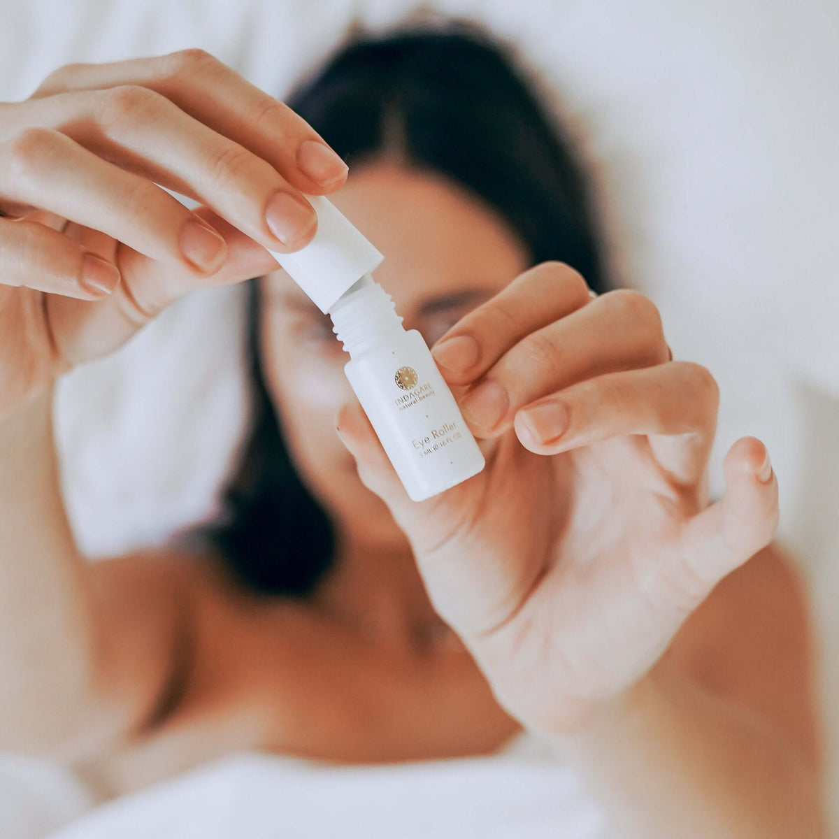 Woman lying in bed holding up the Prickly Pear Seed Oil eye roller