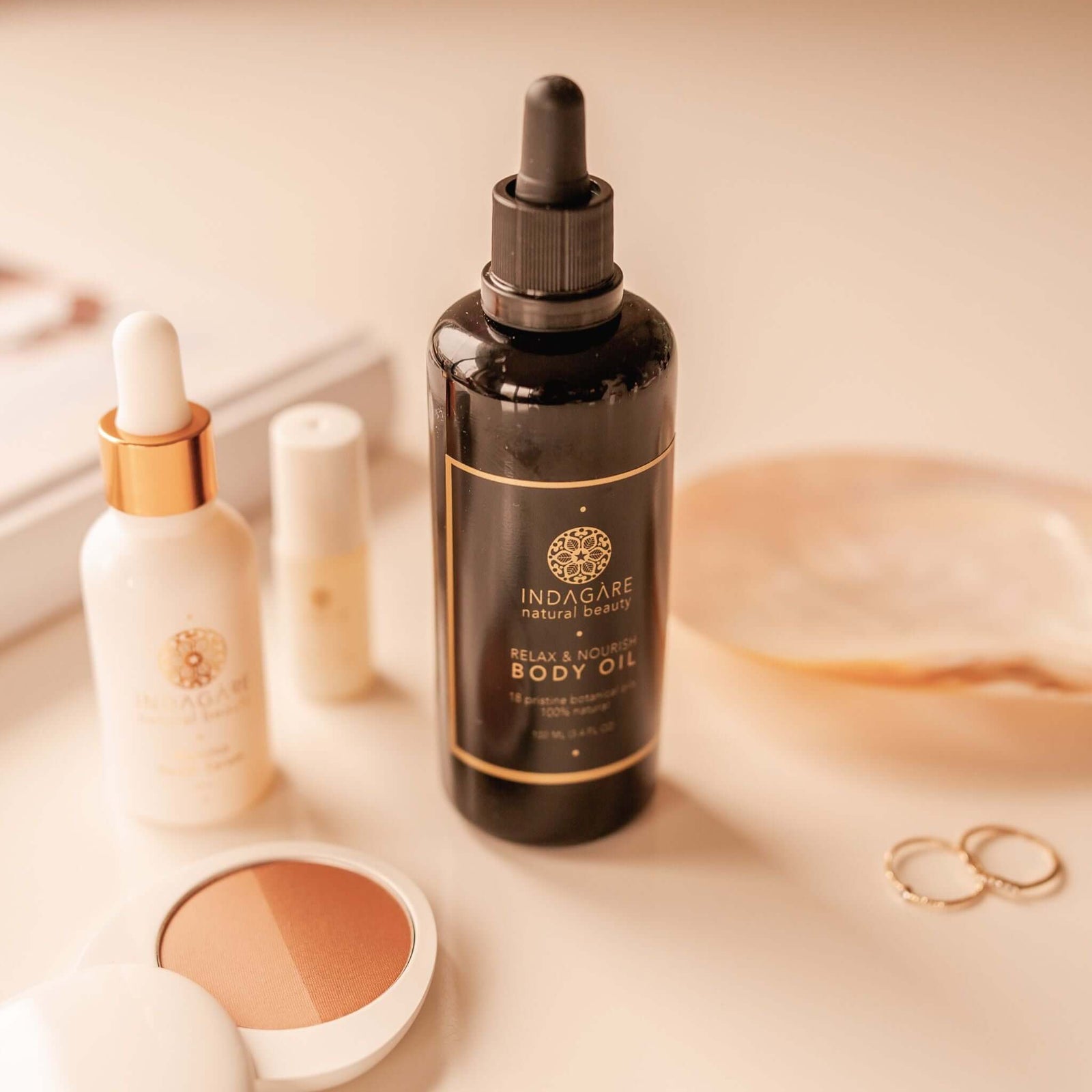 Indagare's Relax and Nourish Organic Body Oil displayed on a bathroom vanity with hair oil and makeup products